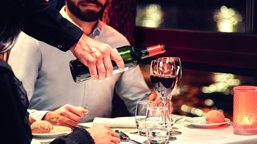 Waiter pouring wine on Maxim's Seine River Cruise dining table.