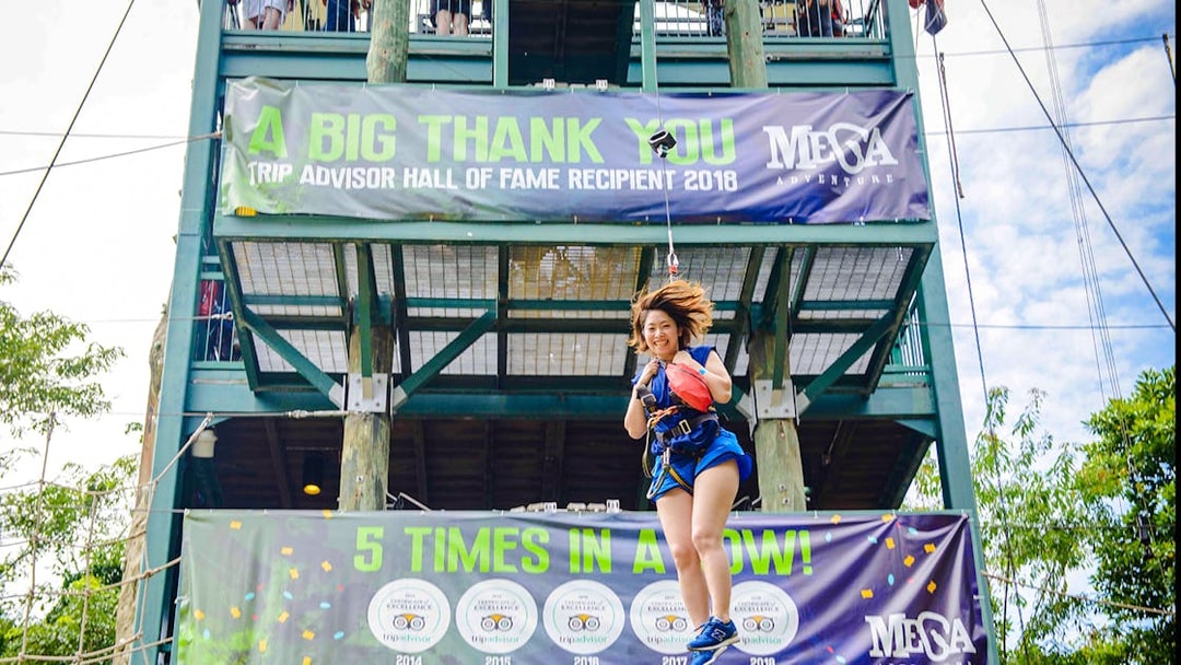 Person ziplining at Mega Adventure Park, Singapore, with banners in the background.