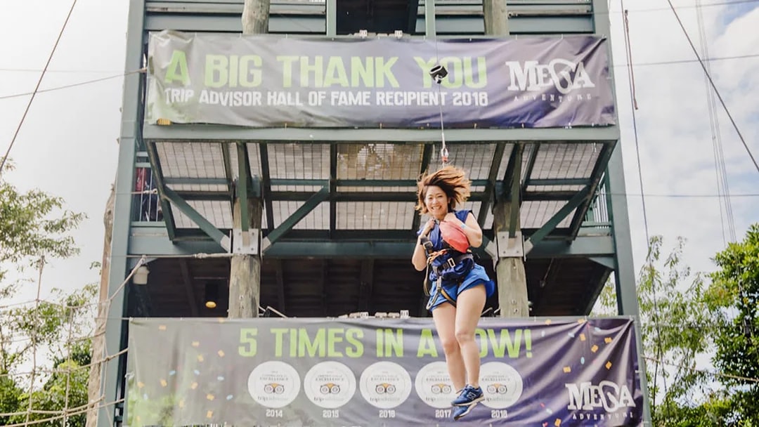 Person ziplining at Mega Adventure Park, Singapore, with award banners in the background.