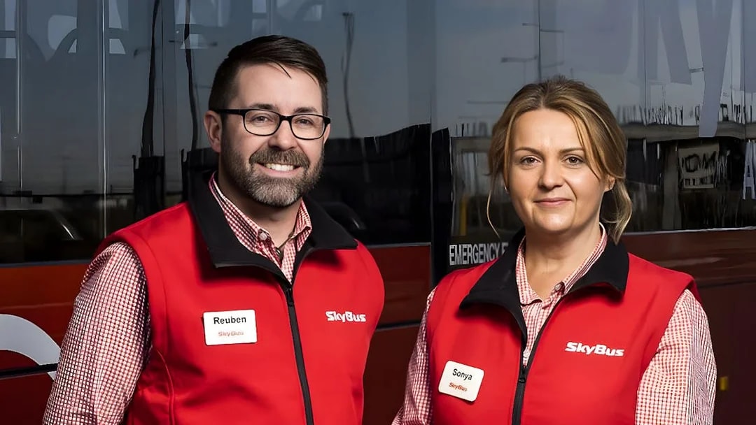 Skybus staff in red vests standing in front of Melbourne Airport shuttle bus.