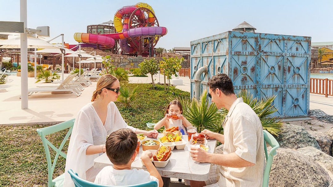 Visitors enjoying a meal at Meryal Waterpark with colorful slides in the background.