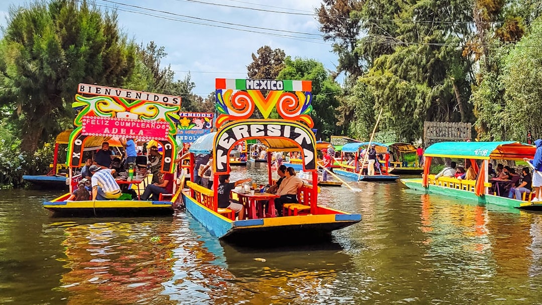 Colorful trajineras on Xochimilco canals, Mexico, with people enjoying a boat tour.