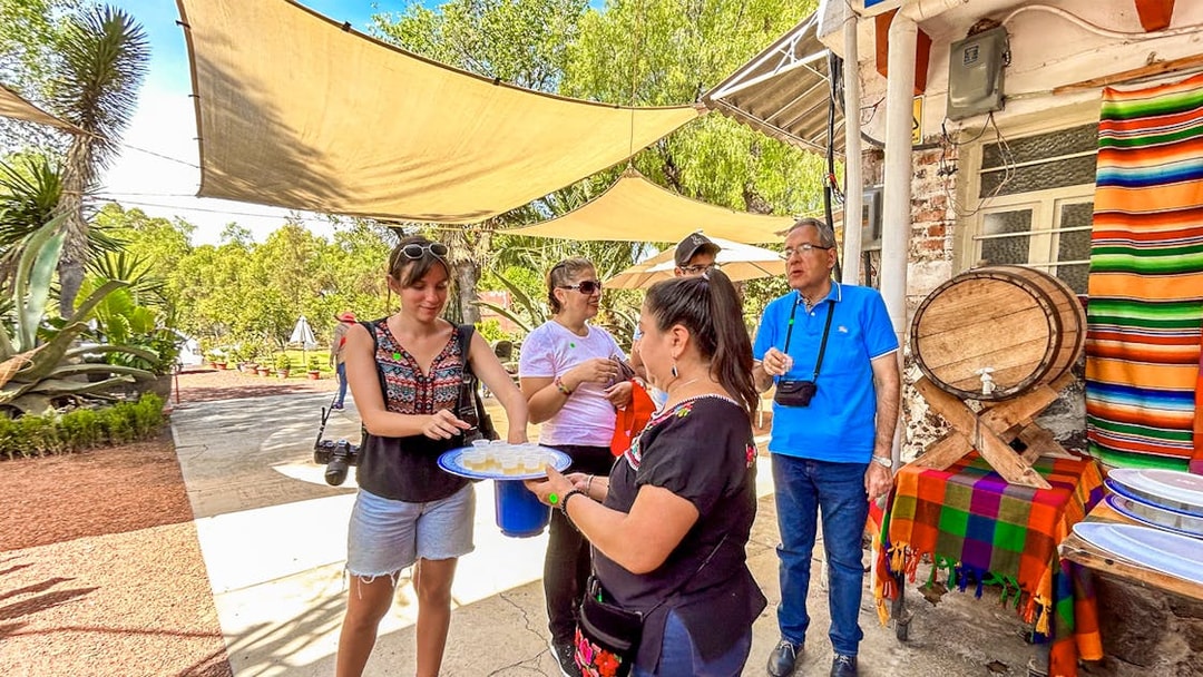 Tourists sampling tequila outdoors near a colorful table and barrel in Mexico.