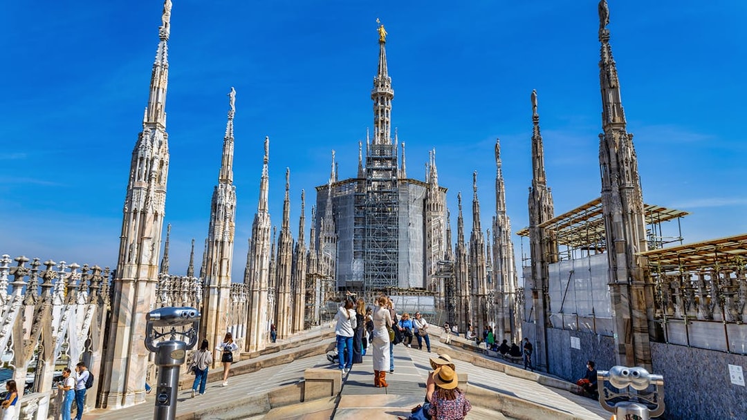 Tourists exploring the rooftop of Milan Duomo with spires in view.
