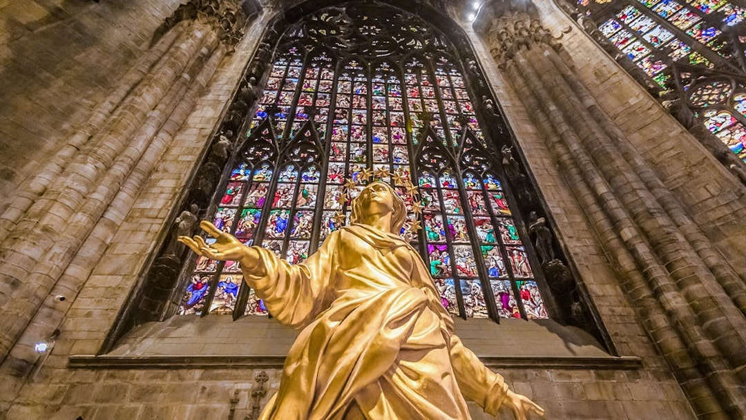 Golden statue and stained glass inside Duomo Cathedral, Milan.