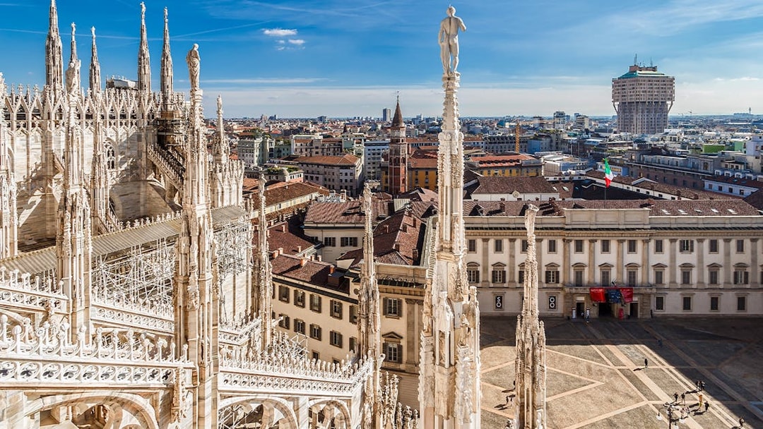 Milan Cathedral rooftop view with cityscape and Italian flag.