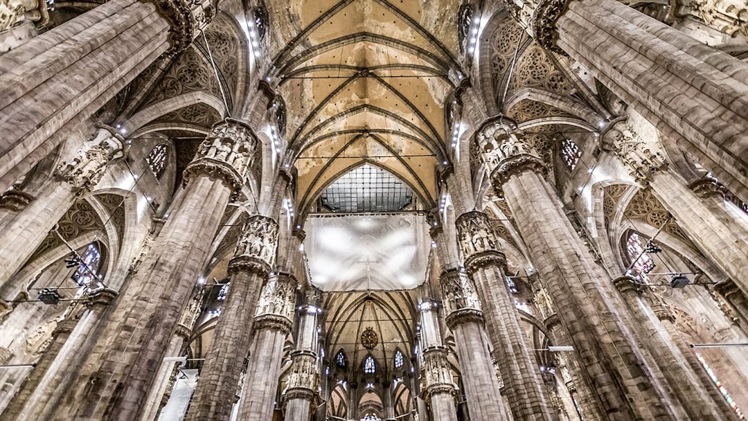 Interiors of Duomo Cathedral in Milan showcasing ornate columns and vaulted ceilings.
