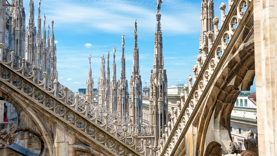 Statues atop spires of Milan Cathedral Duomo under blue sky.