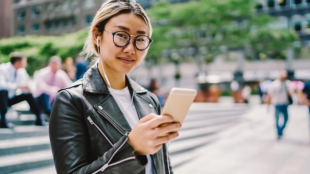 Asian woman using audio guide on smartphone in urban setting.