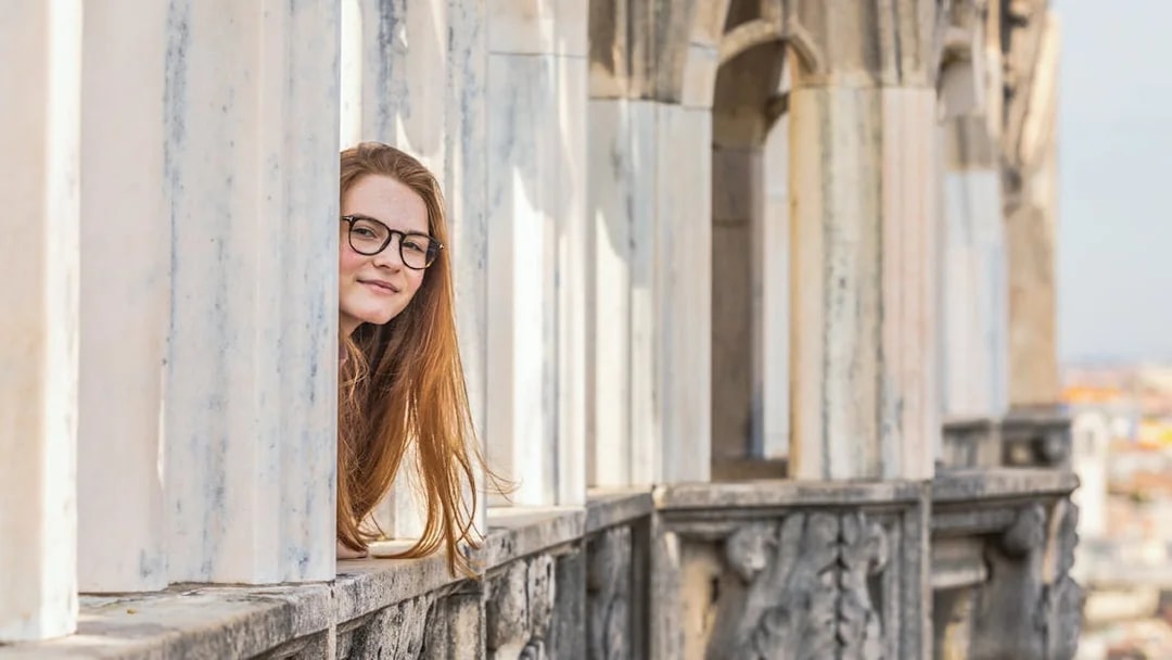 Person peeking through marble columns on Milan Duomo rooftop.