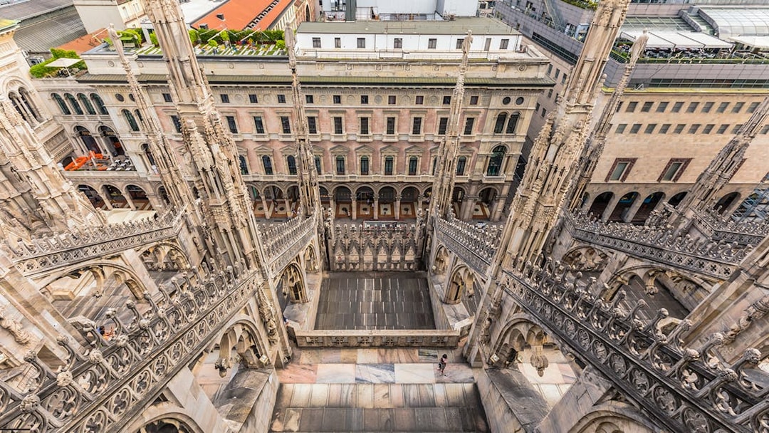 Rooftop view of Milan Duomo Cathedral's intricate spires overlooking city buildings.