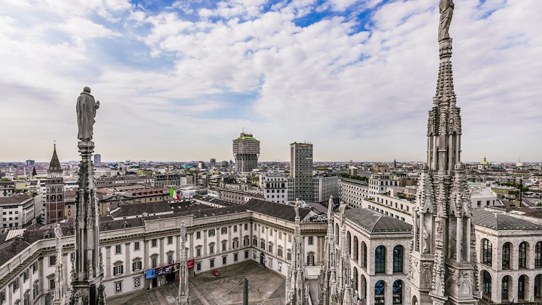 Aerial view of Milan cityscape from Duomo Cathedral rooftop, featuring spires and historic buildings.