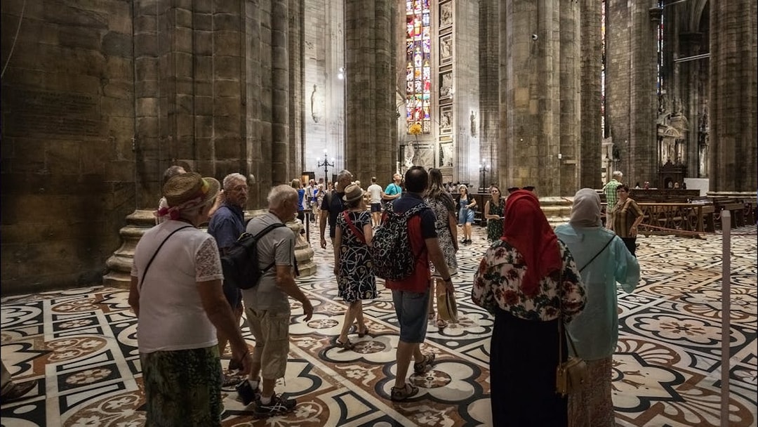 Tourists inside Duomo di Milano admiring stained glass windows and architecture.