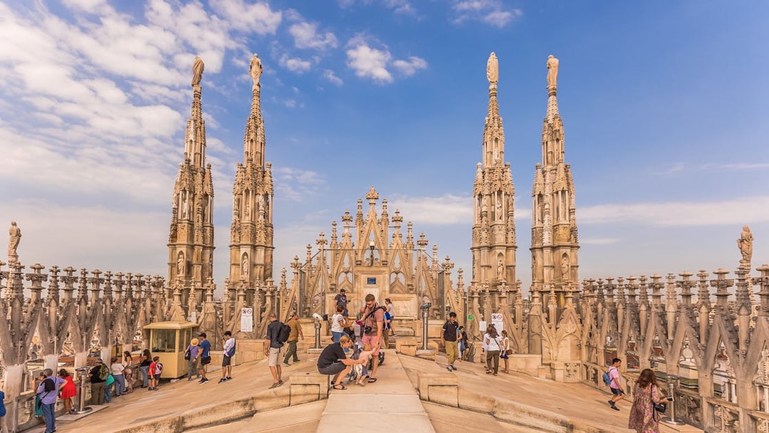 Visitors exploring the rooftop spires of Milan Duomo Cathedral under a clear sky.