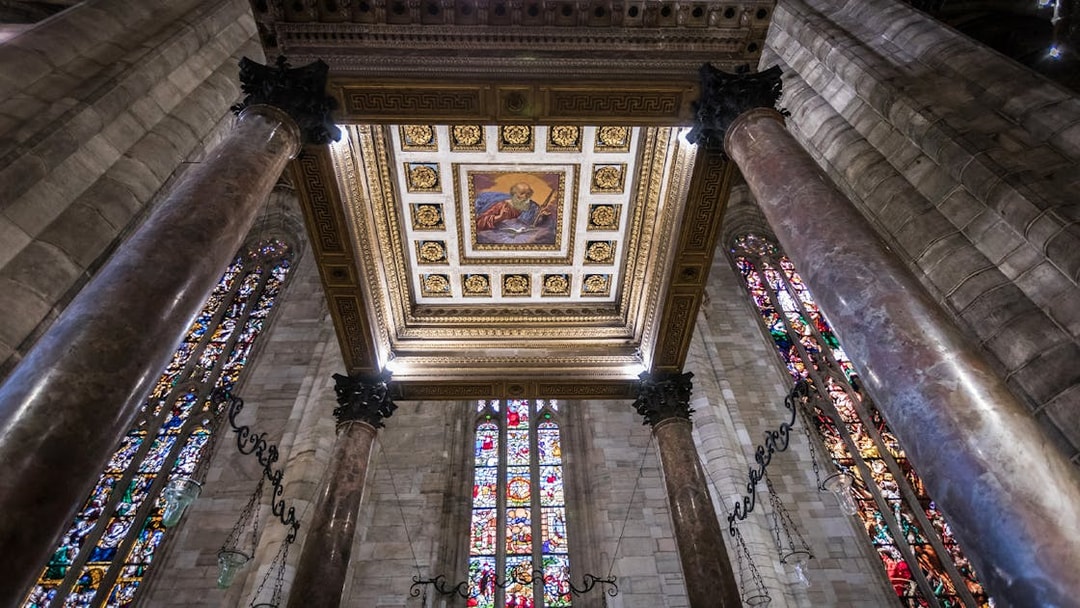 Interior view of Milan Duomo ceiling with stained glass windows and ornate columns.
