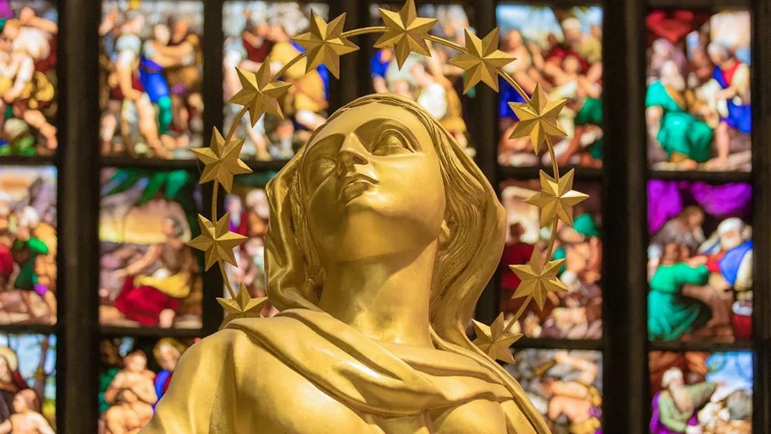 Golden statue inside Milan Duomo Cathedral with stained glass backdrop.