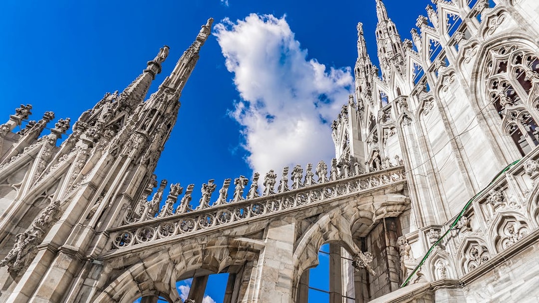 Duomo Cathedral rooftop spires and ornate architecture against blue sky, Milan, Italy.