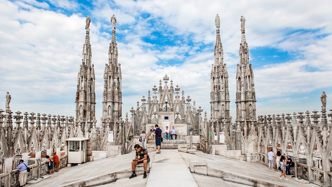 Tourists exploring rooftop of Duomo Cathedral, Milan with spires in view.