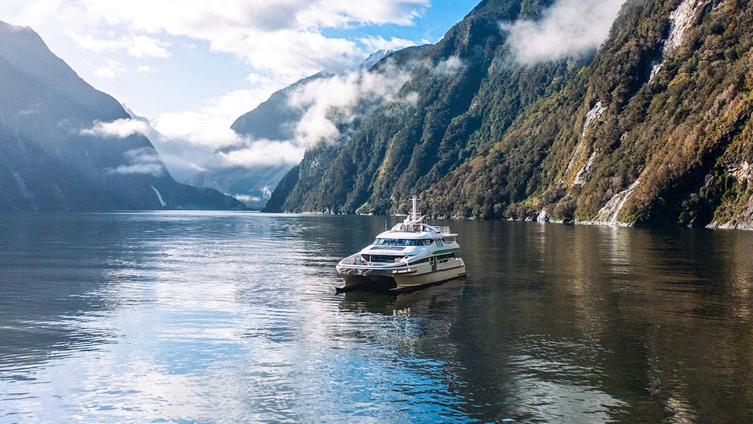 Cruise boat on Milford Sound surrounded by misty mountains and calm waters.