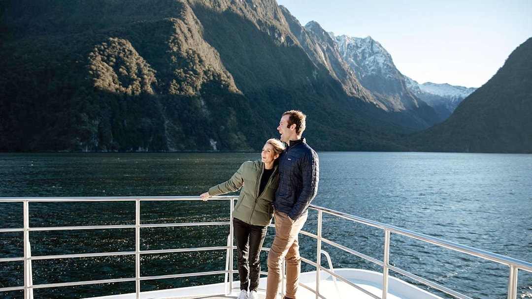 Couple on a boat enjoying Milford Sound's scenic mountain views.