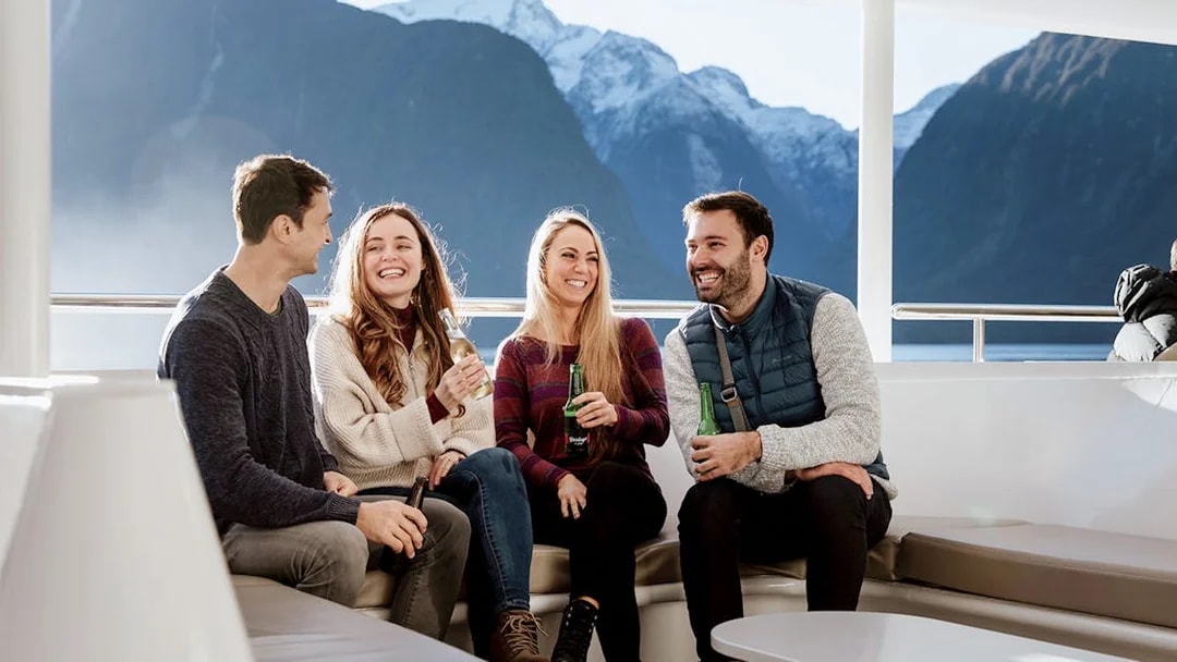 Group enjoying drinks on a Milford Sound cruise with scenic mountain views.