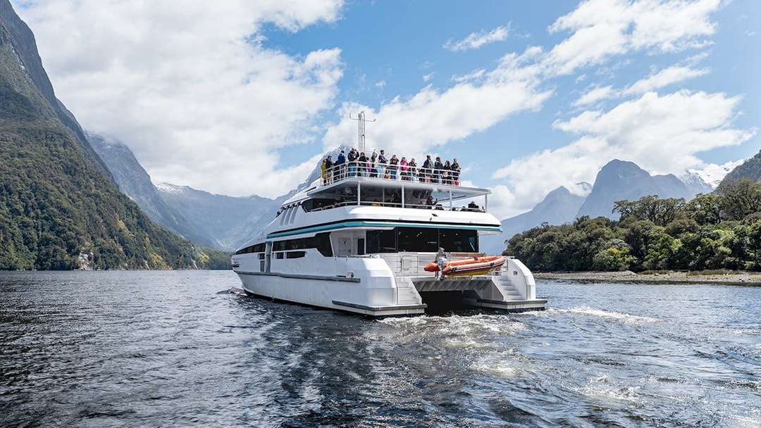 Cruise boat on Milford Sound with passengers viewing scenic mountains.