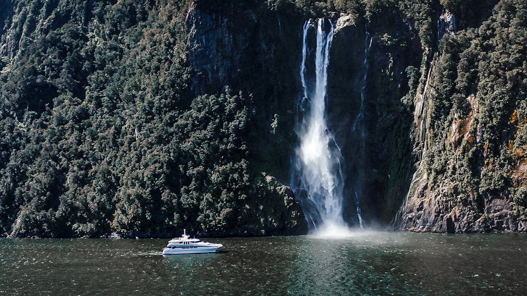 Cruise boat near waterfall in Milford Sound, New Zealand.