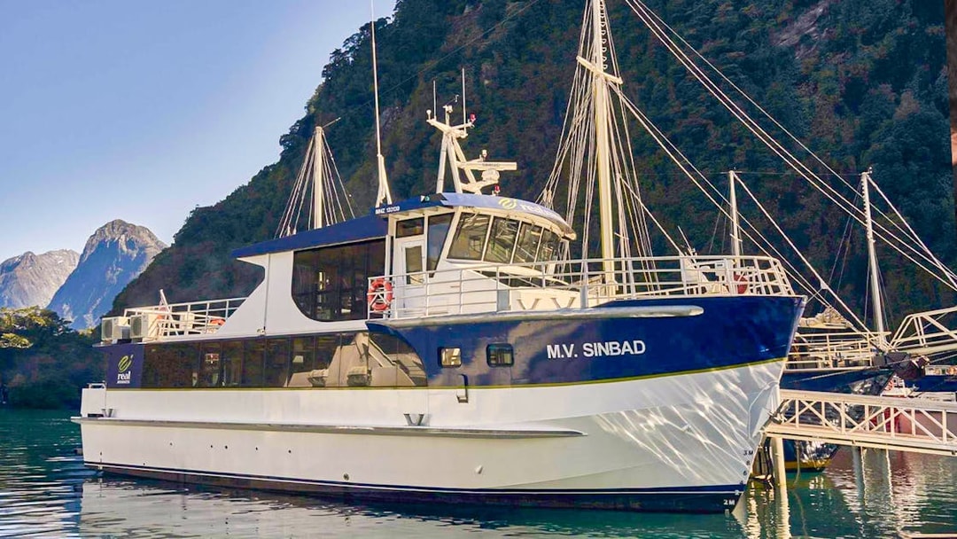 Cruise boat docked at Milford Sound with scenic mountain backdrop.