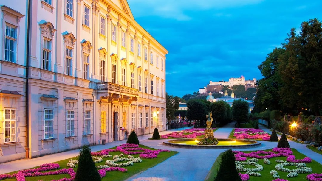 Mirabell Palace gardens at dusk, Salzburg, with Hohensalzburg Fortress in the background.