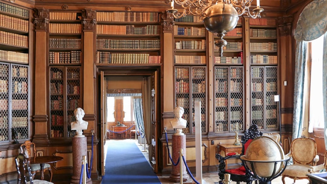 Miramare Castle reading room with bookshelves, busts, and a globe.