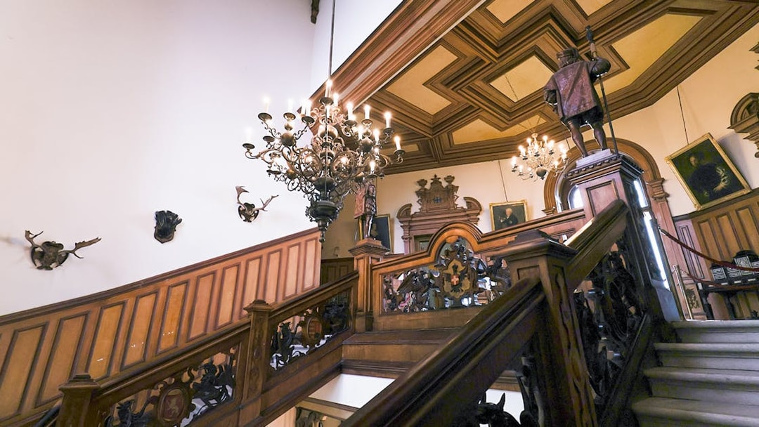 Miramare Castle staircase with ornate woodwork and chandeliers leading to the upper floor.