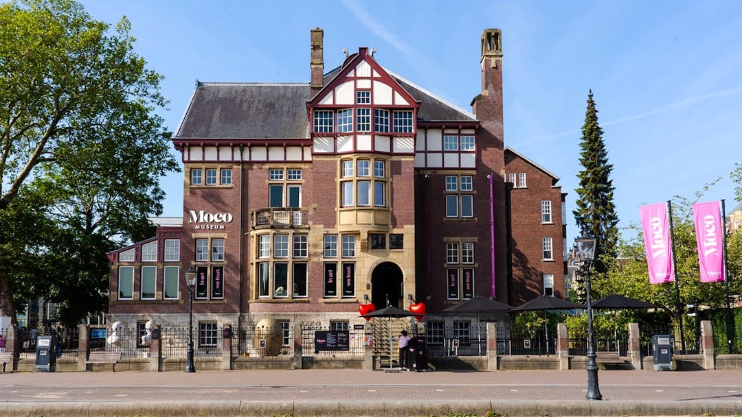 Exteriors of Moco Museum in Amsterdam with historic architecture and pink banners.