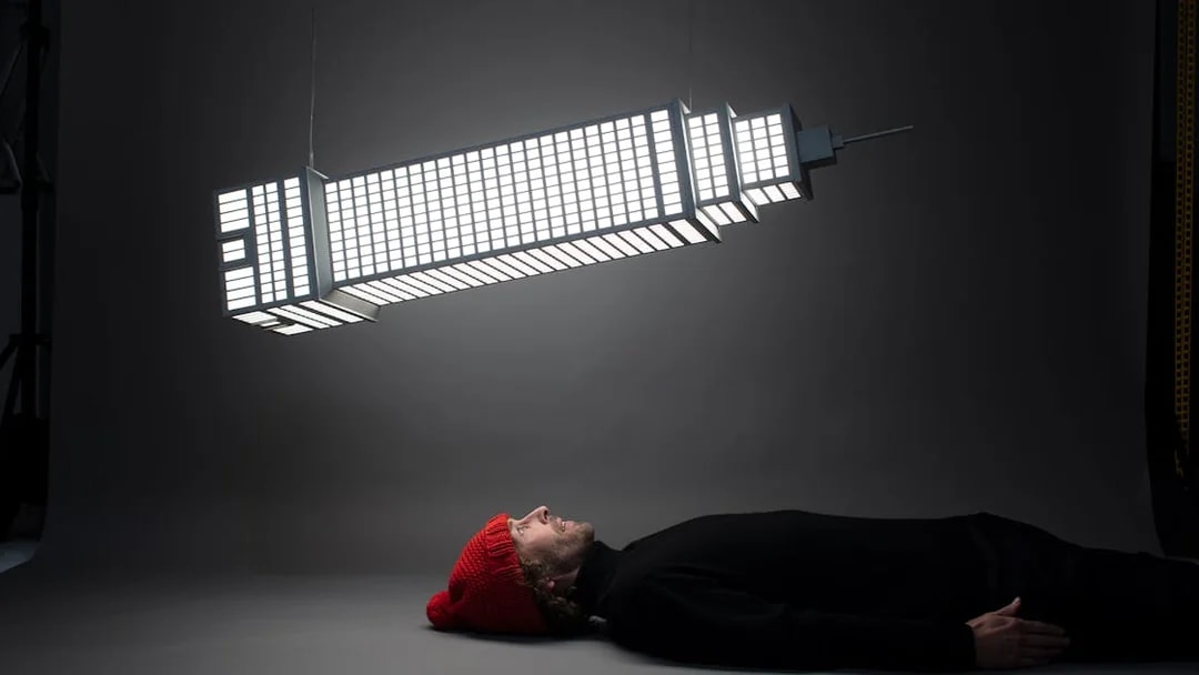 Man lying beneath illuminated sculpture at Amsterdam Moco Museum's Planet Positive Disruption exhibit by Frankey.