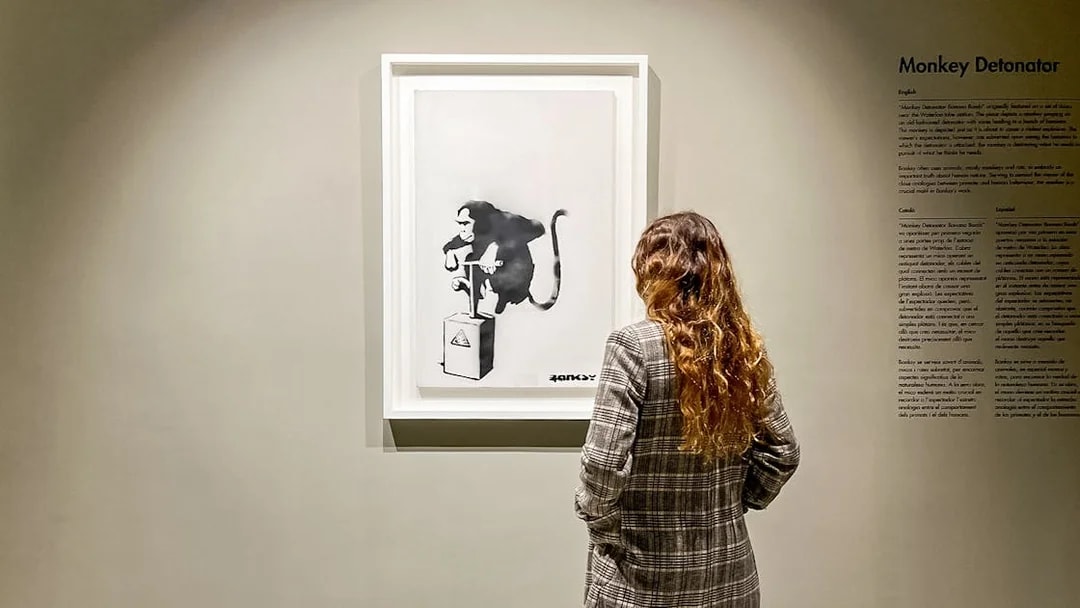 Tourist viewing Banksy's "Monkey Detonator" artwork in a gallery.