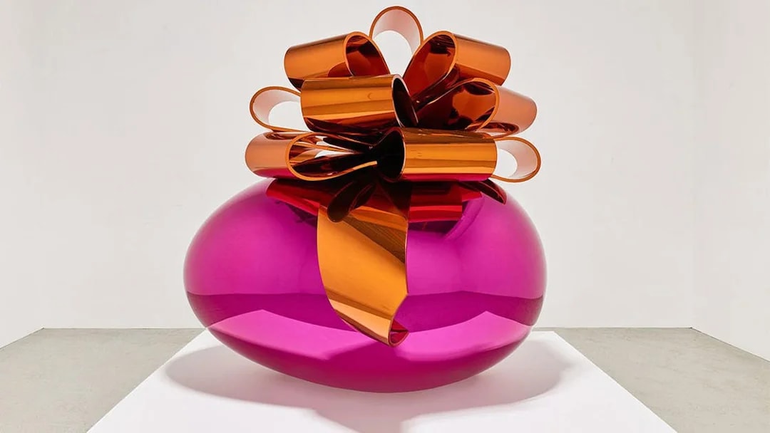 Sculpture of a large pink metallic egg with an orange bow at Moco Museum London exhibit.