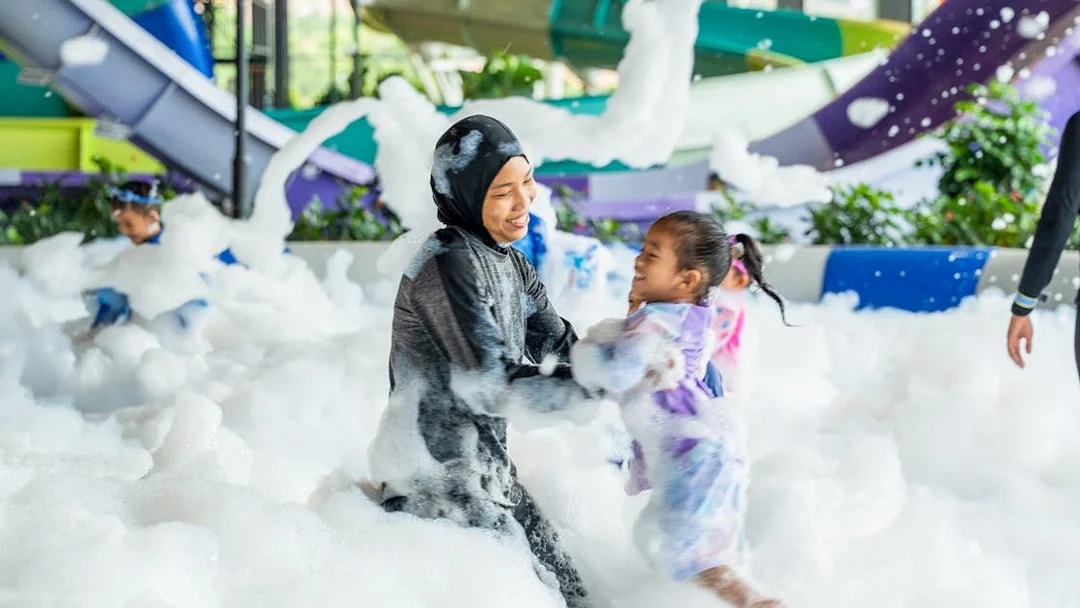 Woman and child playing in foam at a water park splash zone.