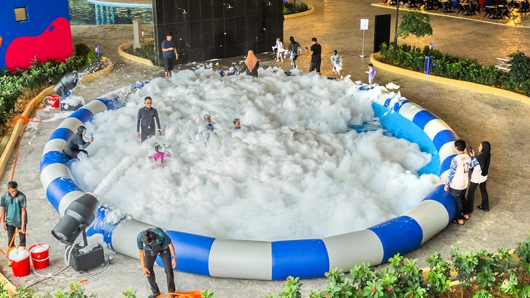 Kids and adults enjoying foam in a splash zone at an indoor water park.