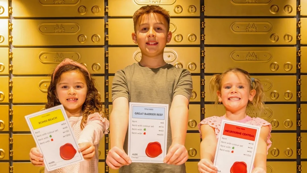 Children holding Monopoly property cards at Monopoly Dreams Melbourne exhibit.
