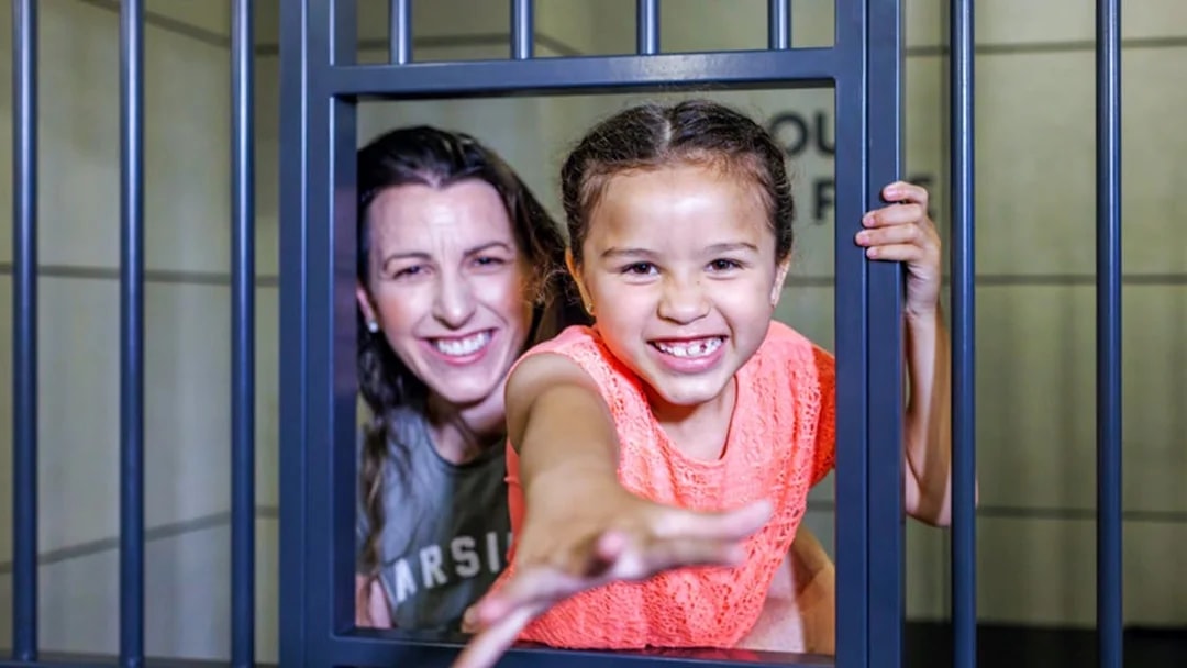 Child and adult smiling behind bars at Monopoly Dreams Melbourne.
