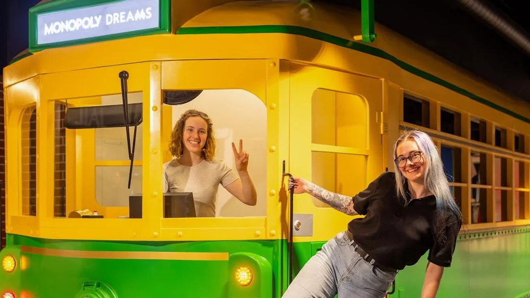 Monopoly Dreams Melbourne tram exhibit with two smiling visitors.