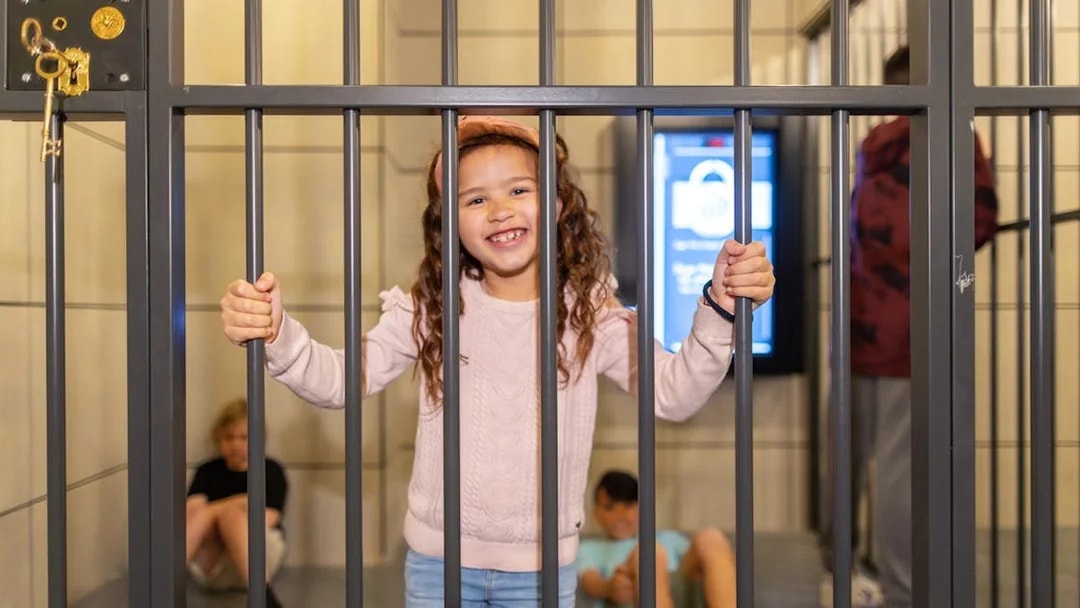 Child smiling behind bars at Monopoly Dreams Melbourne attraction.