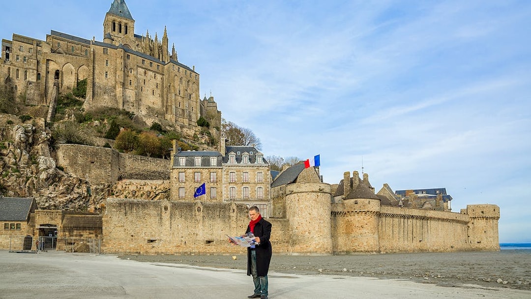 Visitor reading map in front of Mont-Saint-Michel Abbey, France.