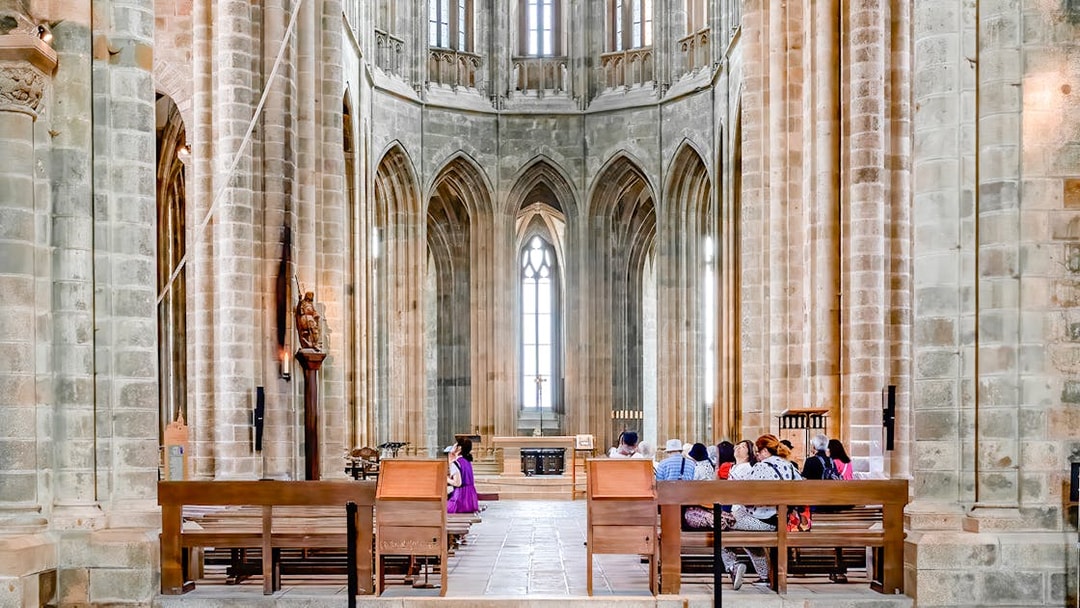 Visitors seated inside Mont-Saint-Michel Abbey, France, admiring Gothic architecture.