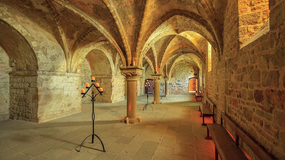 Mont-Saint-Michel Abbey interior with stone arches and candlelit stands.