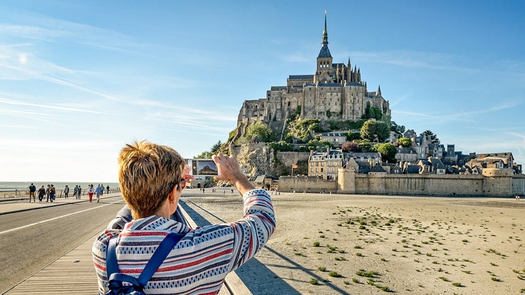 Visitor photographing Mont Saint-Michel with smartphone, France.