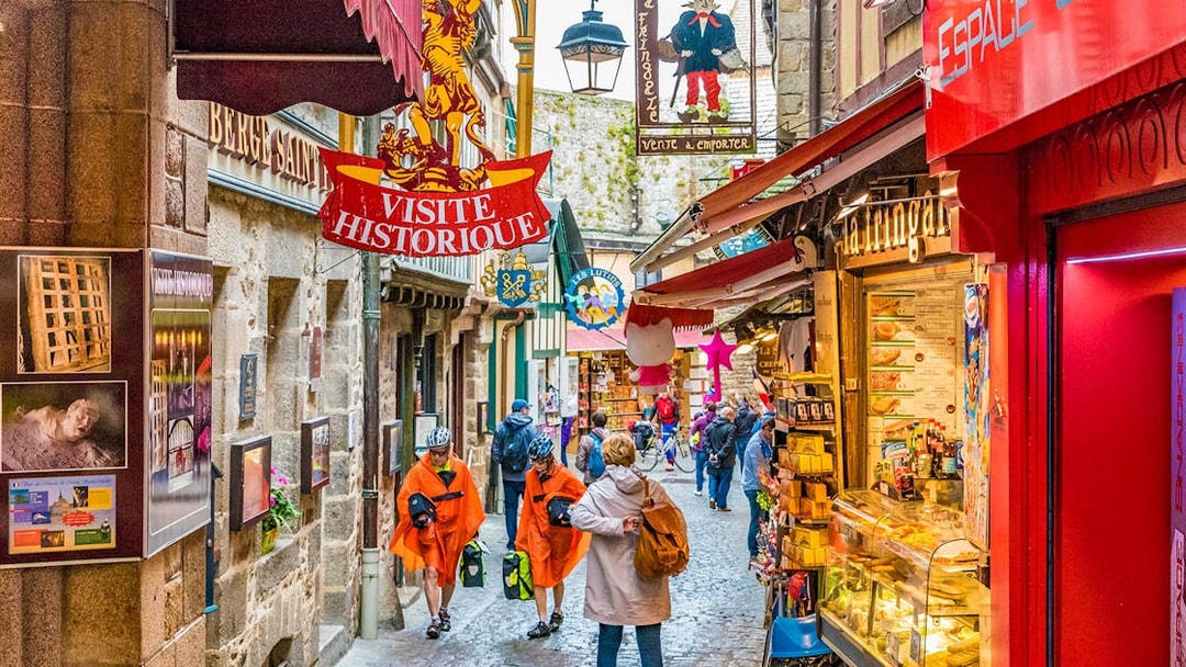 Narrow street in Mont Saint-Michel with tourists and historic shop signs.