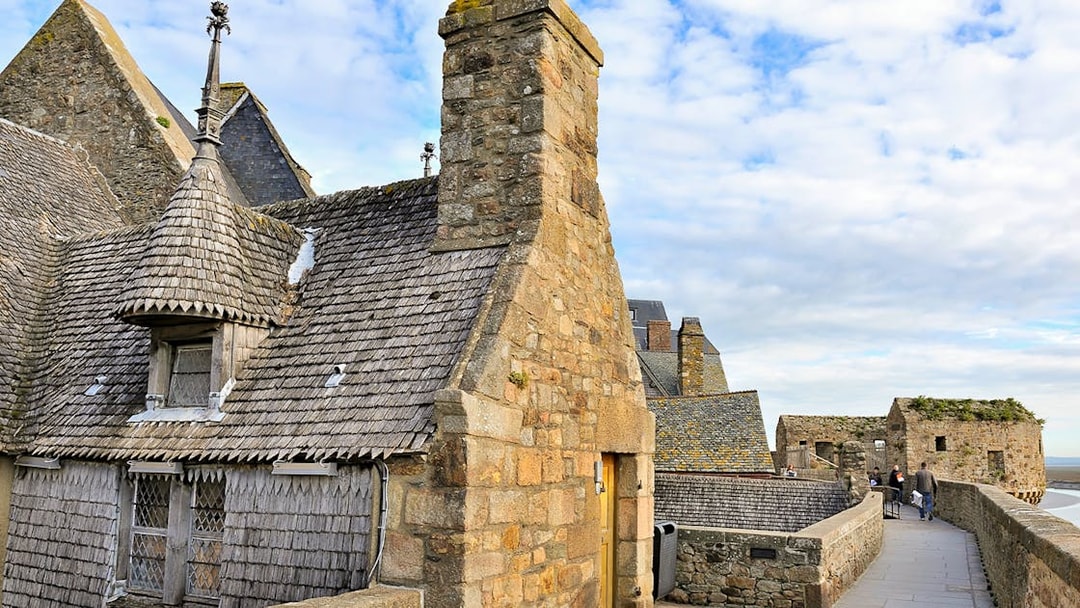 Remparts of Mont Saint Michel with stone buildings and walkway under a blue sky.