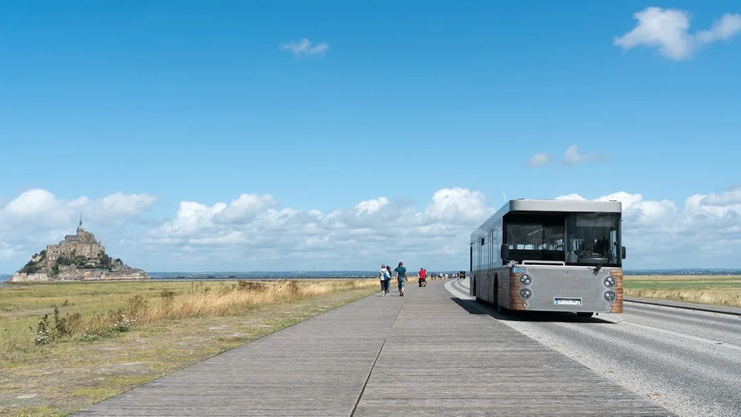 Tourist bus approaching Mont Saint-Michel, France, on a clear day.