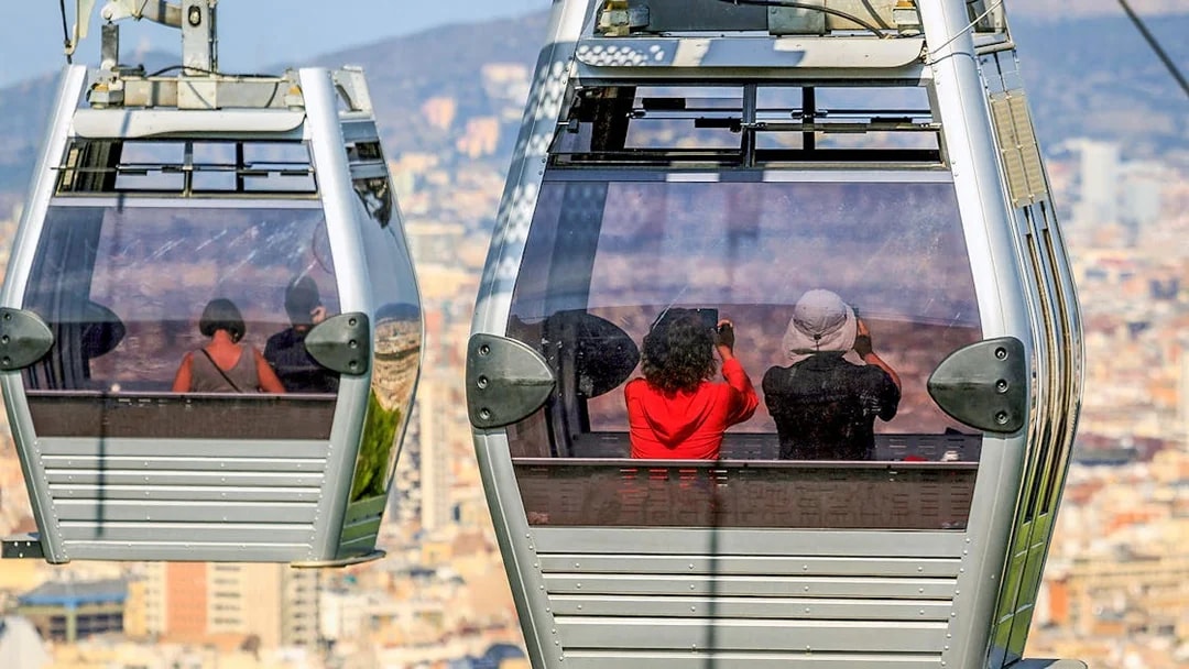 Montjuic cable cars with passengers overlooking Barcelona cityscape.