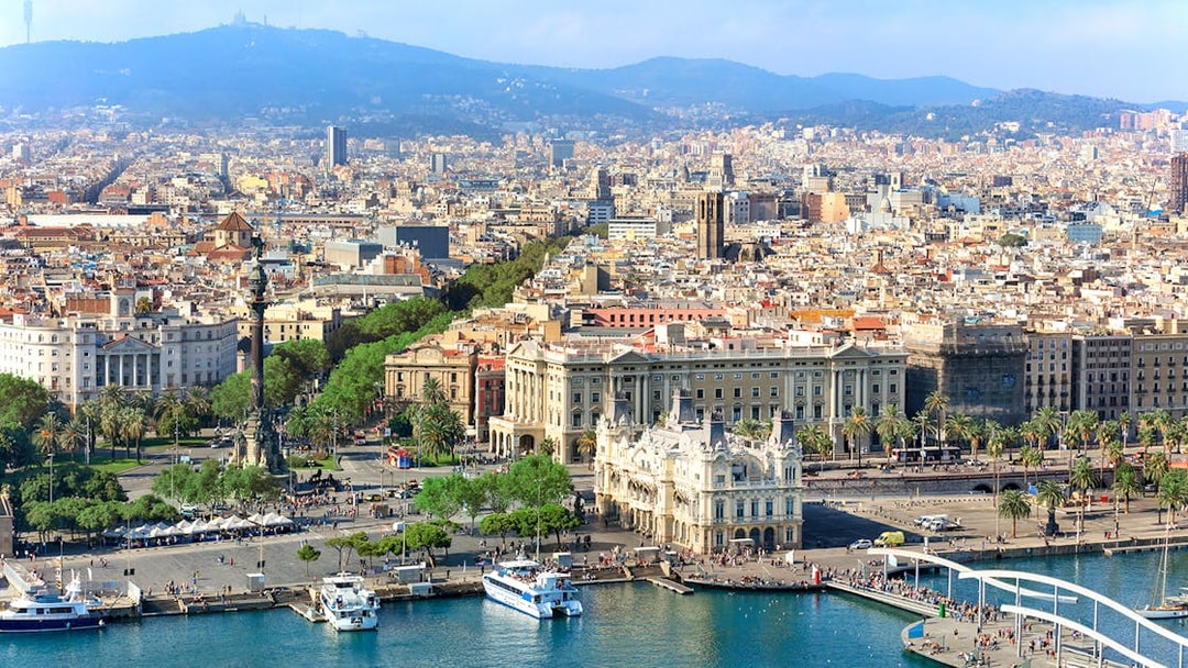 Aerial view of Barcelona's waterfront and cityscape, featuring Montjuic in the background.